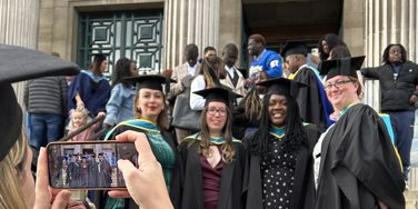 Graduation - graduate wearing cap and gown taking photos of a group of smiling graduates