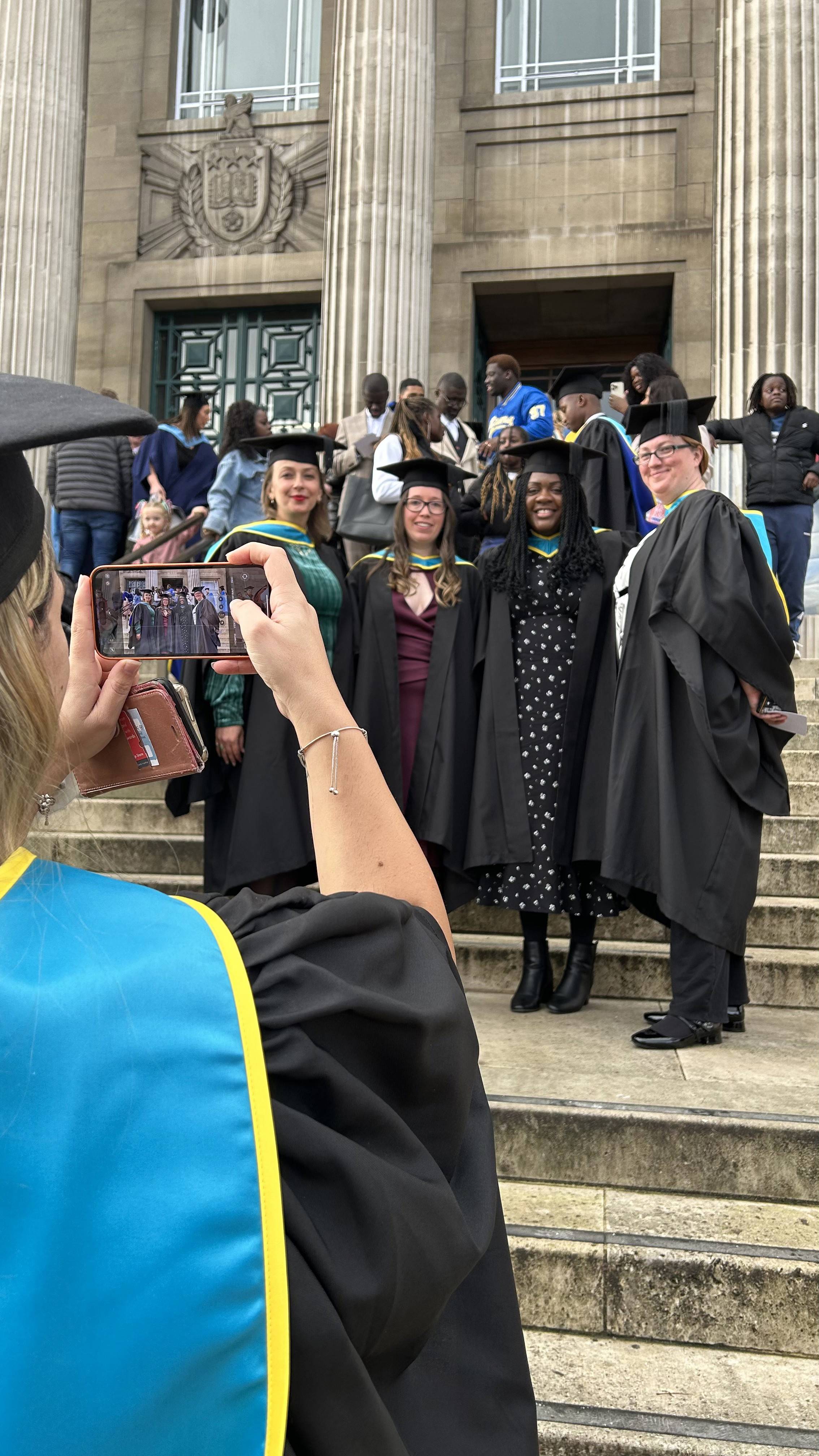 Graduation - graduate wearing cap and gown taking photos of a group of smiling graduates